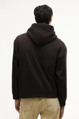 Canguro color marrón oscuro, de corte holgado, con capucha forrada y cordón ajustable. Presenta hombros caídos, bolsillo canguro y remates acanalados en puños y bajo.