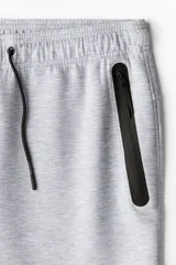 Pantalón de jogging deportivo color gris claro, de corte ajustado (slim fit), confeccionado en tejido funcional DryMove™ que absorbe el sudor. Presenta cintura elástica con cordón de ajuste negro y bolsillos laterales con cierre sellado negro.