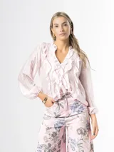 Camisa de organdí rosa pastel con finas rayas verticales metalizadas, escote en V con volados frontales y mangas largas abullonadas con puños elásticos.