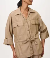 Campera tipo parka de la marca Marfinno, confeccionada en mezcla de algodón, viscosa y lino en color beige. Presenta cuello camisero, cierre frontal con botones, bolsillos con solapa en el pecho y cintura ajustable con cordón y lazo. Las mangas son largas con puños abotonados.