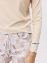 Polera de cuello alto confeccionada en tela rib color blanco, con mangas largas y hombreras. Presenta pespuntes en contraste en las terminaciones del cuello, hombros y puños.