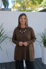 Sweater de tejido de punto en color chocolate, con corte holgado, cuello redondo y mangas largas. Presenta un diseño con bolsillos frontales integrados y terminaciones acanaladas en puños y ruedo.