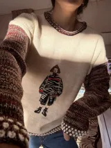 Sweater tejido con cuerpo en color crudo y mangas en lana multicolor. Presenta un diseño frontal estampado estilo vintage y detalles de tejido a crochet en cuello y puños.