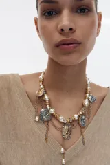 Collar de diseño maximalista compuesto por una cadena de perlas y esferas metálicas doradas, adornado con múltiples dijes colgantes que incluyen medallas grabadas, un camafeo central, corazones y cadenas finas plateadas y doradas.