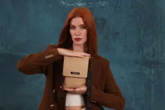 Phonebag pequeña color mostaza, confeccionada en cuero sintético, con solapa frontal y correa ajustable con logo de la marca.