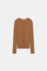 Chaqueta de punto marrón con cuello redondo, manga larga y ribetes en color rojo. Cuenta con cierre frontal de botones.