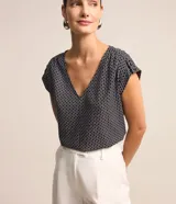 Blusa de crepé con estampado geométrico en blanco y negro, escote en V y mangas cortas sin sisa con detalle fruncido en los hombros.