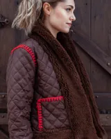 Campera acolchada de diseño artesanal, con detalles de piel sintética en cuello, puños y ruedo. Presenta costuras decorativas en crochet color rojo en los bolsillos y hombros, con cierre frontal.