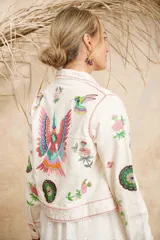 Campera de algodón color blanco con estampado de flores, plumas y colibríes, cuello camisero y cierre frontal con botones.