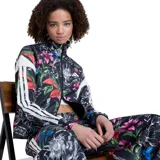 Campera deportiva Adidas Farm Tiro para mujer, de color negro con estampado floral multicolor. Presenta cuello alto, cierre frontal completo y las clásicas franjas blancas de la marca en las mangas.