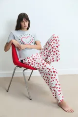 Pijama compuesto por una remera gris de manga corta con estampa central de corazón y un pantalón largo blanco con estampado de corazones rojos y frases.