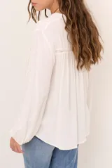 Camisa color natural de manga larga, con escote en V y detalles de encaje o calados decorativos en el frente y las mangas. Cierre frontal con botones.
