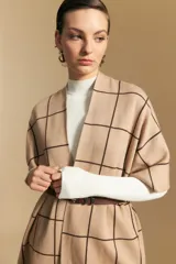 Poncho abierto de tejido de punto con estampado de cuadros en tonos beige y líneas oscuras. Presenta un diseño versátil ideal para superponer sobre otras prendas.
