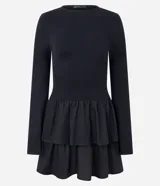 Vestido corto negro de viscosa con mangas largas, cuello redondo y falda godê con superposición de volantes. La parte superior es acanalada y la inferior tiene capas fruncidas.