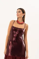 Vestido corto de tirantes finos en color bordó con acabado metalizado brillante. Presenta un corte recto ajustado al cuerpo y un detalle de volado en el ruedo confeccionado en tela traslúcida.