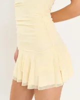 Vestido corto strapless color amarillo pastel, con diseño ajustado al cuerpo y falda con volados en el ruedo.