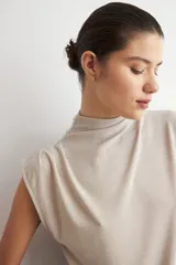 Blusa de lurex negra sin mangas, con cuello alto drapeado y detalle de pliegues frontales.