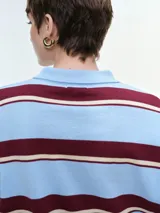Buzo tejido de punto a rayas horizontales en tonos marrón, rojo y crema, con cuello polo y cierre frontal de botones. Presenta mangas largas con puños elastizados y un corte holgado.