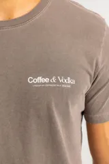 Remera de algodón color marrón con efecto lavado, cuello redondo y estampa pequeña en el pecho con la frase Coffee & Vodka.