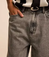Bermuda de jean estilo baggy, color negro gastado, con bolsillos, cierre de botón y cremallera, y pespuntes contrastantes.