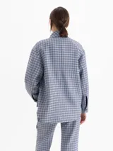 Chaqueta de twill en tono celeste con estampado de cuadros, corte camisero y largo por debajo de la cadera. Presenta cuello clásico, cierre frontal con broches forrados en cuero y bolsillos frontales tipo cargo.