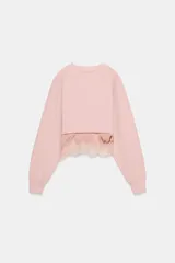 Sudadera crop de cuello redondo y manga larga con puños elásticos. Presenta un diseño de doble capa con un top interior satinado y un bajo decorado con encaje a tono.