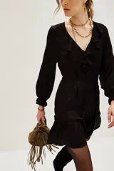 Vestido corto color negro, con escote en V decorado con volados, mangas largas con puños elásticos y falda con volado en el ruedo. Incluye un lazo para ajustar en la cintura.