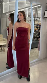 Vestido largo strapless bordó con sutil brillo, diseño entallado con fruncido frontal y tajo lateral.