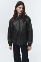 Chaqueta estilo bomber de cuero marrón oscuro, con cuello alto, cierre frontal de cremallera, dos bolsillos frontales con solapa y puños y bajo acanalados.