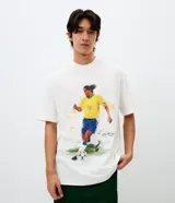 Remera de algodón con corte relaxed, cuello redondo y mangas cortas. Presenta un estampado frontal con una ilustración estilo acuarela de Ronaldinho jugando al fútbol.