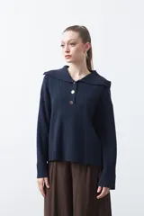 Sweater de tejido de punto color azul marino, con cuello polo amplio y cierre frontal con tres botones metálicos. Presenta mangas largas levemente acampanadas y un diseño de silueta relajada con aberturas laterales en el ruedo.