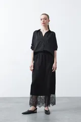 Falda midi negra de caída fluida con cintura elastizada y un amplio detalle de encaje negro en el bajo.