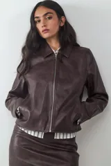 Chaqueta de cuero sintético efecto lavado en color marrón, de corte recto, con cuello camisero, cierre frontal de cremallera metálica y bolsillos laterales.