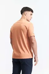 Remera de manga corta color salmón, con escote redondo y un pequeño estampado frontal de una flor azul sobre un fondo texturizado, con la inscripción "MISTRAL ® 1976 INTERNATIONAL".