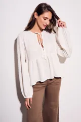 Blusa color crudo de viscosa y lino con bordados en el frente, escote con lazo y mangas largas. Corte holgado con frunce en la cintura.