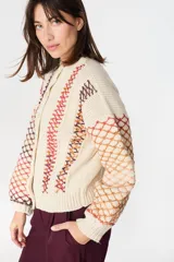 Saco de punto artesanal en color crudo, con diseño de red multicolor en mangas y laterales. Presenta cuello redondo, cierre frontal con botones y puños acanalados.