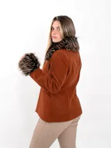 Chaqueta corta color beige confeccionada en lana, con cuello y puños de piel sintética en tonos marrones y negros. Presenta cierre frontal con botones y bolsillos laterales.