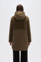 Campera de diseño híbrido en color verde oliva, que combina paneles de corderito en la parte superior y capucha con una sección inferior acolchada con diseño de rombos. Cuenta con cierre frontal, botones a presión y bolsillos frontales con solapa.