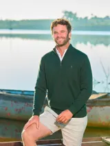 Sweater de tejido de punto fino en color azul marino, con diseño de medio cierre frontal y cuello alto. Presenta puños y ruedo acanalados, con un pequeño bordado distintivo en el pecho.