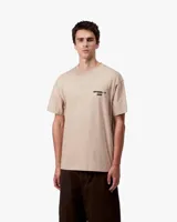 Remera de manga corta color beige, con cuello redondo y un pequeño estampado negro en el pecho izquierdo con texto.