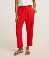 Pantalón de crepé rojo, modelo estilo pijama, de corte fluido, con cintura elástica y lazo de ajuste con terminales metálicas. Cuenta con bolsillos laterales y cierre frontal con cremallera y botón.