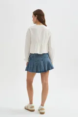 Minifalda de jean negra con diseño cruzado, cierre de hebilla metálica y detalle de tablones plisados en el lateral.
