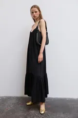 Vestido midi de color negro, confeccionado en tejido fluido, con escote en V y tirantes finos ajustables. Presenta frunces en el pecho y un volante en el bajo.