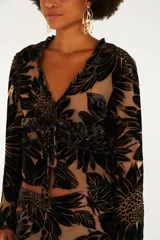 Blusa de manga larga con escote en V, cierre frontal con lazos ajustables y terminaciones de volados en cuello y puños. Confeccionada en tejido semitransparente con diseño floral aterciopelado.