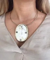 Gargantilla con aro rígido plateado y dije ovalado con textura marmolada en tonos blanco y beige, con detalles metálicos plateados.