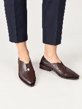 Mocasines de charol color bordó, de diseño vanguardista con corte asimétrico en el empeine, abertura en V, punta fina y suela plana con pequeño tacón.