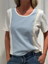 Remera de manga corta con diseño bicolor, combinando paneles frontales en celeste y laterales en blanco. Presenta detalles de puntilla decorativa en las costuras y un corte asimétrico, siendo más corta en la parte delantera y más larga en la trasera.