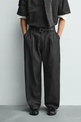 Pantalón de jeans de algodón ligero, color negro lavado, con corte balloon fit (holgado y ancho). Presenta pliegues frontales marcados en la cintura y cierre frontal de cremallera y botón.