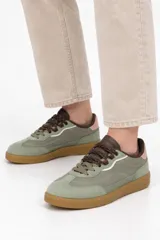 Zapatilla deportiva estilo urbano de corte bajo, color verde con suela de goma marrón y cordones oscuros.