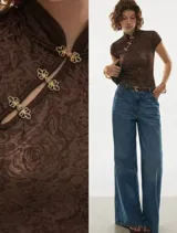 Top de encaje floral color chocolate, con cuello estilo mandarín y cierre frontal con broches ornamentales dorados. Presenta un calce ajustado al cuerpo y mangas cortas.